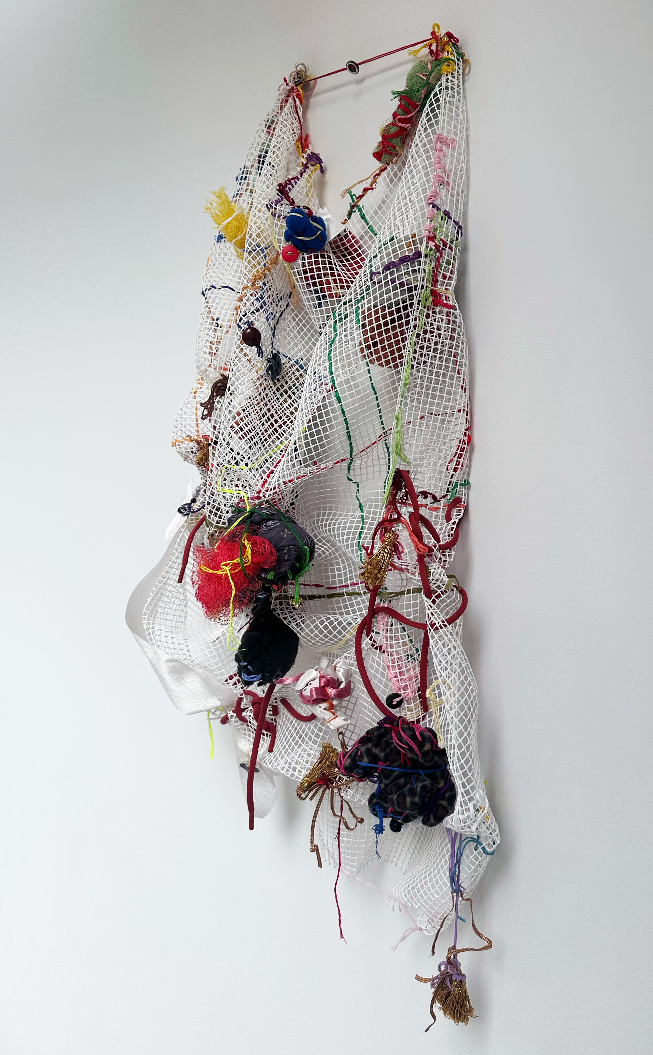 A sculpture made of netting, fabric, and various soft objects hanging on a wall.